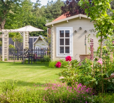 English garden in summer with summerhouse with trees, plants and flowers.