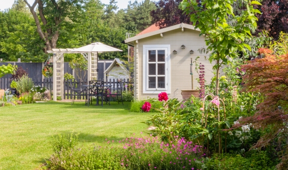 English garden in summer with summerhouse with trees, plants and flowers.